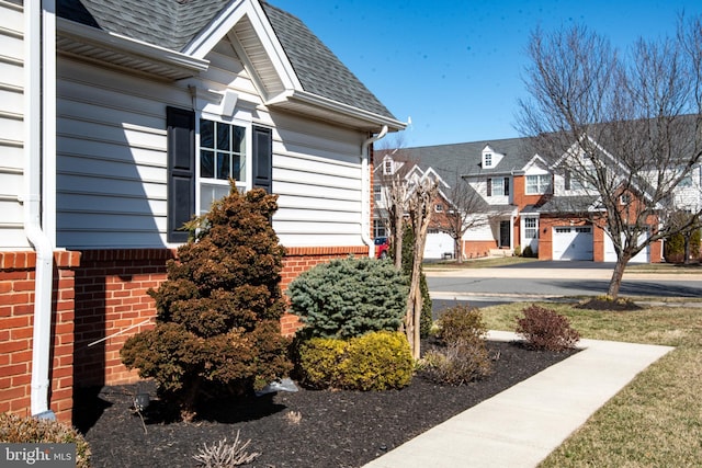 view of property exterior with brick siding, a residential view, and a shingled roof