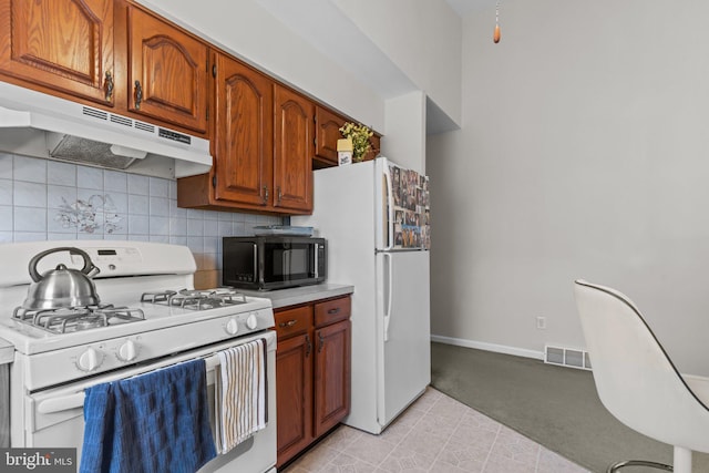 kitchen featuring white appliances, visible vents, light countertops, under cabinet range hood, and backsplash