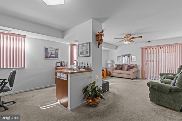 carpeted living area featuring visible vents, a ceiling fan, a sink, baseboards, and a dry bar