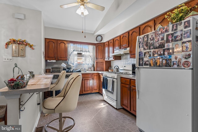 kitchen with under cabinet range hood, backsplash, white appliances, and a kitchen bar