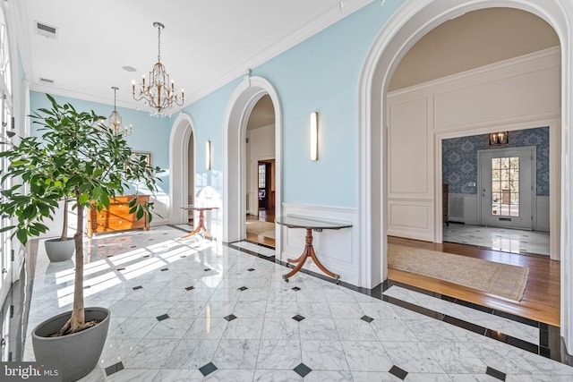 hallway with a notable chandelier, a decorative wall, marble finish floor, and ornamental molding