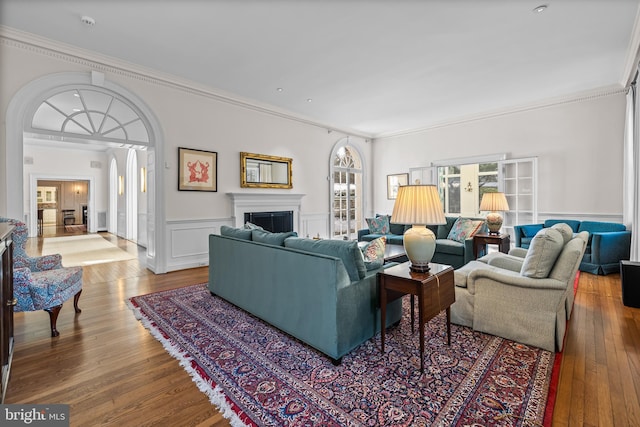 living area with a wainscoted wall, wood finished floors, a fireplace, a decorative wall, and crown molding