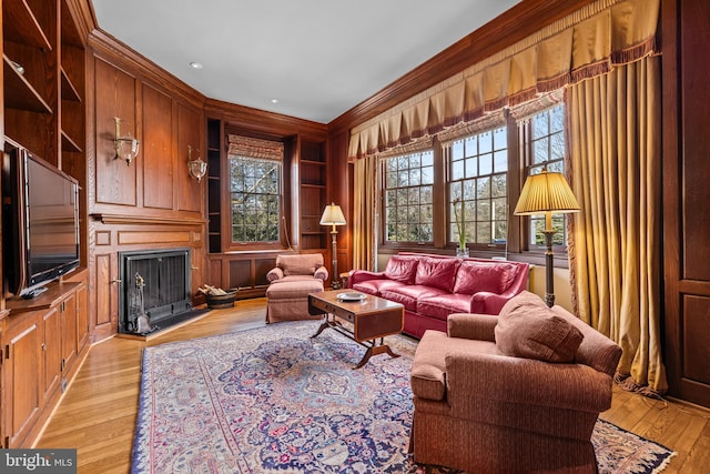 living area featuring light wood-style flooring, built in shelves, crown molding, and wood walls