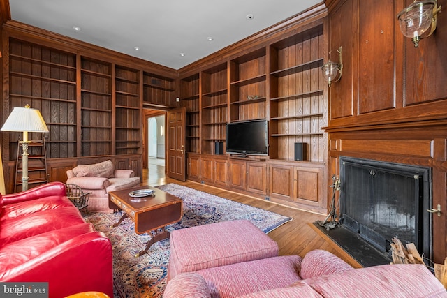 living room featuring a fireplace, wood finished floors, built in shelves, and ornamental molding