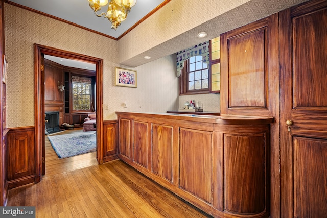 bar featuring a wainscoted wall, a fireplace with raised hearth, ornamental molding, and wallpapered walls