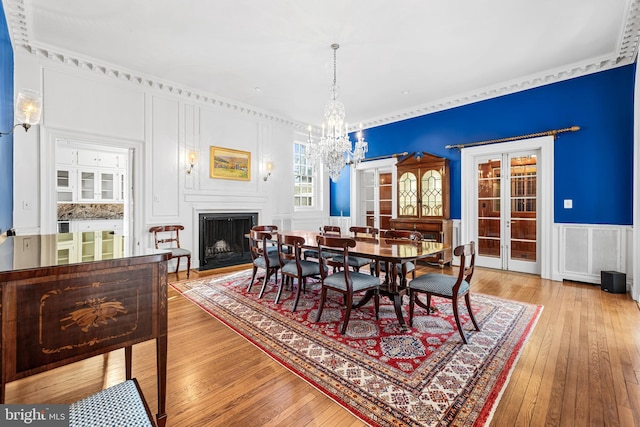 dining area featuring a decorative wall, hardwood / wood-style floors, a fireplace, french doors, and a notable chandelier