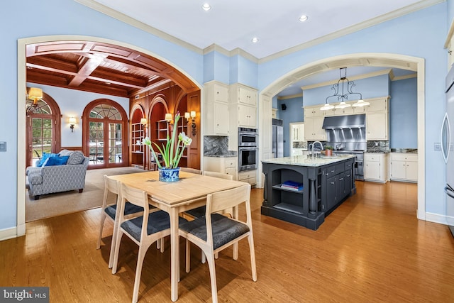 dining space featuring beamed ceiling, coffered ceiling, wood finished floors, arched walkways, and baseboards