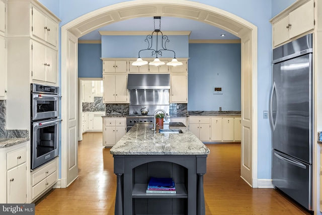 kitchen featuring open shelves, under cabinet range hood, an island with sink, premium appliances, and a sink