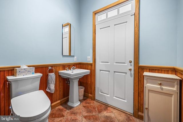 bathroom featuring wooden walls, toilet, a wainscoted wall, and a sink