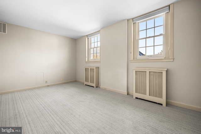 spare room featuring carpet flooring, visible vents, radiator heating unit, and baseboards