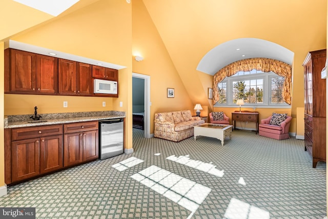 kitchen with white microwave, baseboards, high vaulted ceiling, light colored carpet, and open floor plan