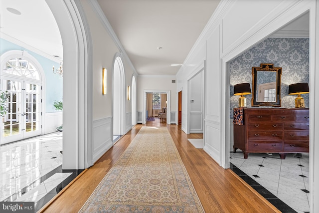 hallway with ornamental molding, a decorative wall, arched walkways, wainscoting, and wallpapered walls