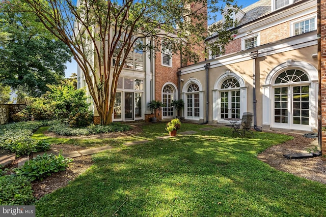 back of house featuring brick siding, a high end roof, stucco siding, french doors, and a yard