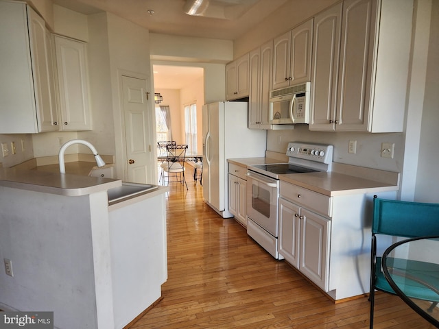 kitchen with light wood-style flooring, a peninsula, white appliances, white cabinetry, and a sink