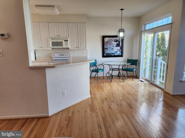 kitchen with white appliances, hanging light fixtures, light countertops, light wood-style floors, and white cabinetry