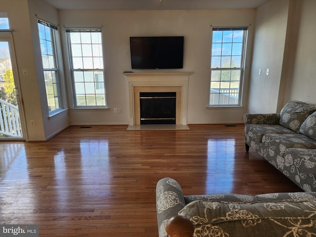 living room with a fireplace with flush hearth, visible vents, baseboards, and wood finished floors