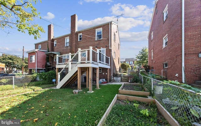 rear view of property with a lawn, fence, stairway, a vegetable garden, and brick siding