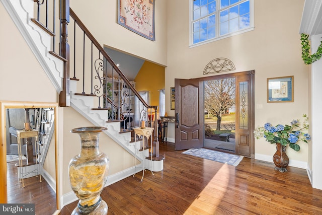 entryway featuring stairs, wood finished floors, baseboards, and a towering ceiling