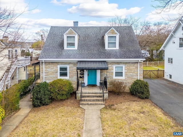 new england style home with a front yard, fence, and a shingled roof