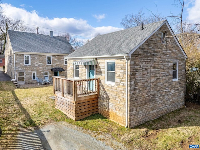 rear view of house featuring a yard, stone siding, and a shingled roof