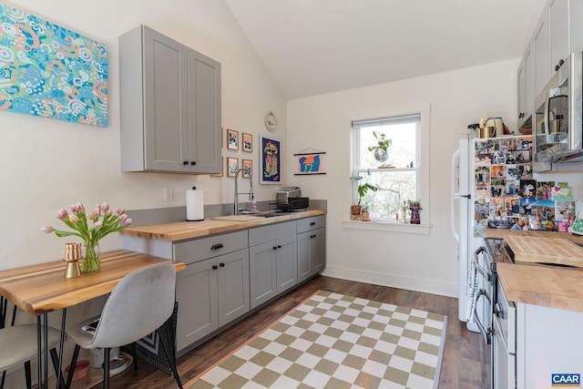 kitchen featuring gray cabinetry, butcher block counters, lofted ceiling, stainless steel appliances, and a sink