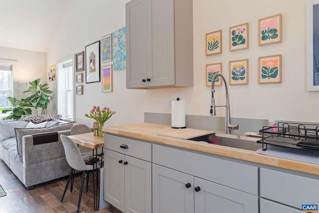 kitchen featuring dark wood-style floors, lofted ceiling, a sink, open floor plan, and butcher block counters