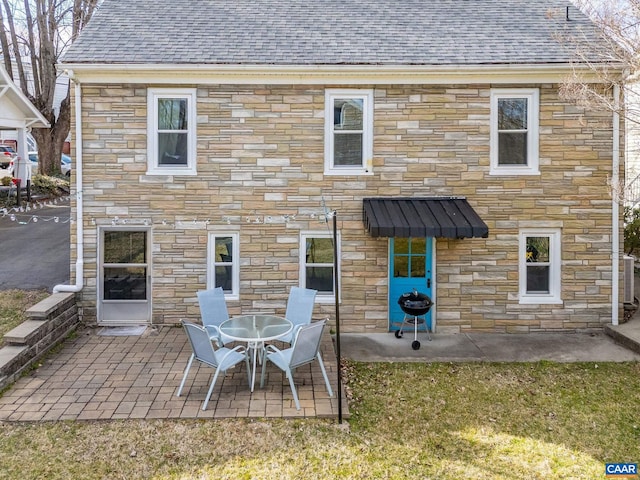 back of property with a patio area, stone siding, and a shingled roof