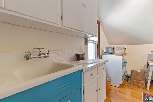 kitchen with white cabinetry, lofted ceiling, light wood-style flooring, and light countertops