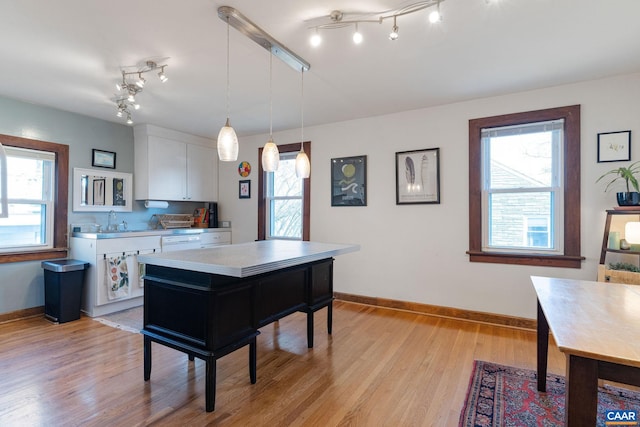 kitchen with pendant lighting, white cabinetry, light wood finished floors, baseboards, and light countertops