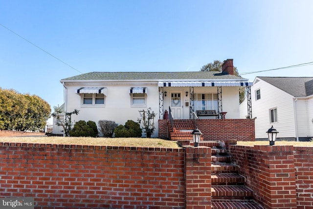 view of front facade featuring stucco siding, roof with shingles, covered porch, and a chimney