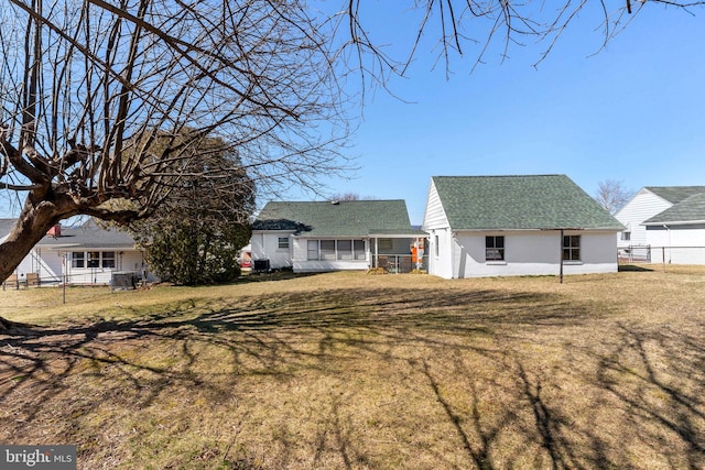 back of property with roof with shingles, a yard, and fence