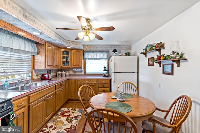 kitchen with freestanding refrigerator, a sink, black range with electric cooktop, glass insert cabinets, and brown cabinets