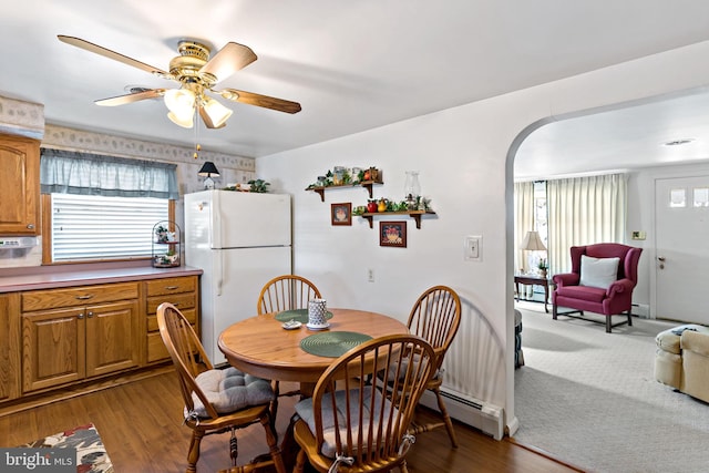 dining space featuring baseboard heating, wood finished floors, arched walkways, and a wealth of natural light