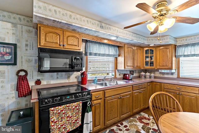 kitchen featuring wallpapered walls, black appliances, brown cabinetry, and a sink