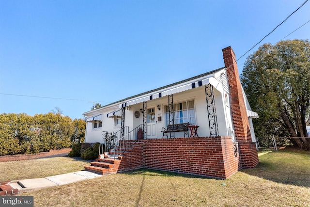 view of front facade featuring brick siding, fence, a front yard, covered porch, and a chimney