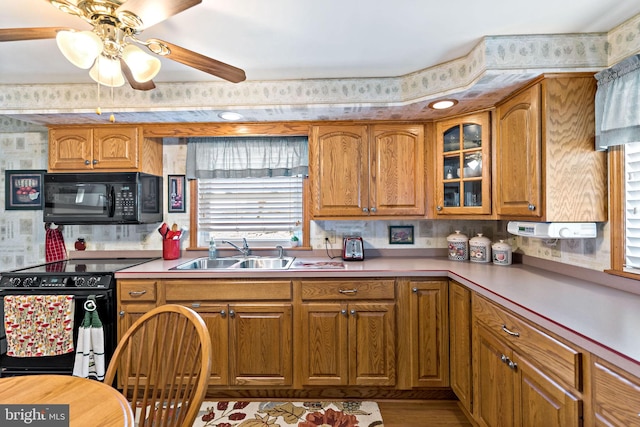 kitchen featuring a sink, black appliances, light countertops, glass insert cabinets, and brown cabinets