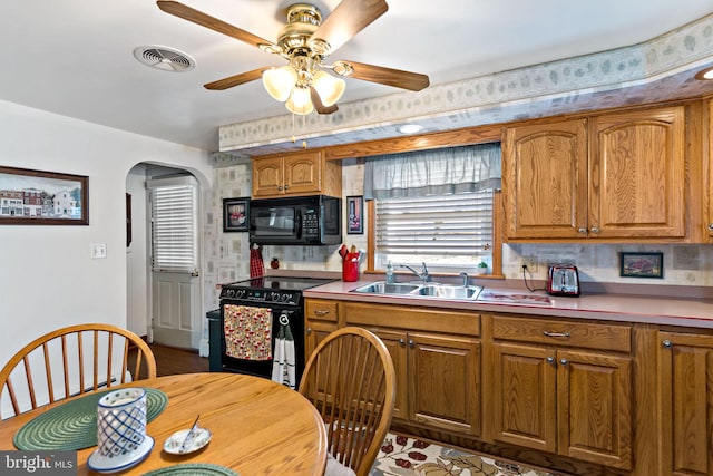 kitchen with brown cabinetry, visible vents, arched walkways, a sink, and black appliances