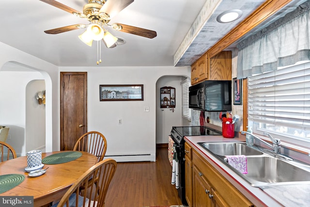 kitchen with arched walkways, a sink, black appliances, dark wood-type flooring, and baseboard heating