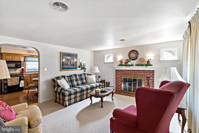 living area featuring a brick fireplace, plenty of natural light, arched walkways, and visible vents