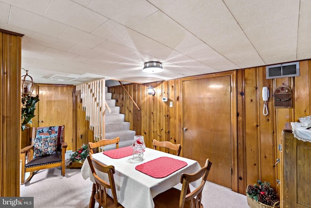 dining area featuring stairway, carpet flooring, visible vents, and wooden walls