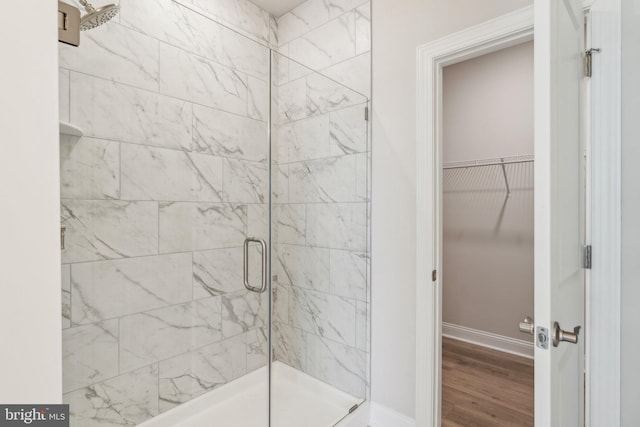 full bathroom featuring a walk in closet, baseboards, wood finished floors, and a shower stall