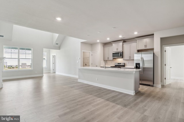 kitchen with light countertops, light wood-type flooring, a center island with sink, and stainless steel appliances