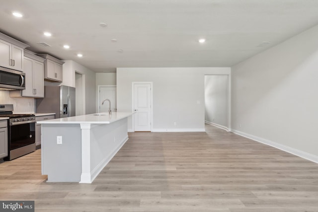 kitchen with a center island with sink, light wood finished floors, a sink, gray cabinetry, and stainless steel appliances