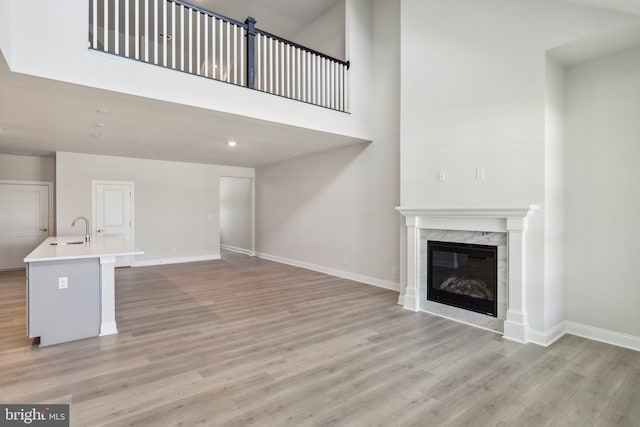 unfurnished living room with baseboards, light wood-type flooring, a high end fireplace, and a sink