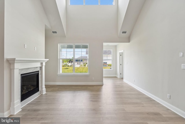 unfurnished living room with visible vents, light wood-style flooring, a fireplace, and a towering ceiling