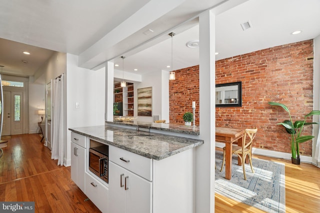 106 15th St SE, Washington, DC 20003 - kitchen featuring stainless steel microwave, wood finished floors, stone countertops, brick wall, and recessed lighting