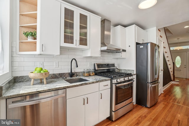 106 15th St SE, Washington, DC 20003 - kitchen featuring stainless steel appliances, wall chimney range hood, white cabinetry, light wood-style flooring, and light stone counters