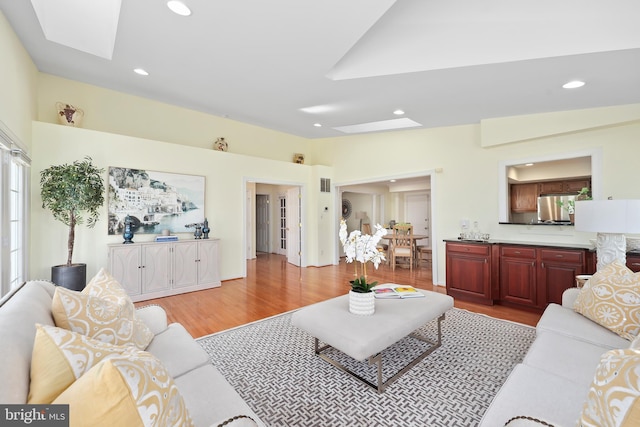 living room featuring lofted ceiling with skylight, recessed lighting, and light wood-type flooring