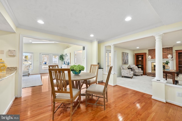 dining room featuring crown molding, light wood-style flooring, a fireplace, and ornate columns