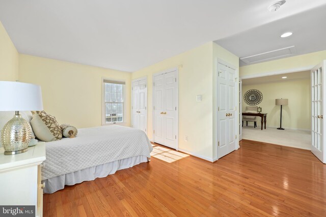 bedroom featuring attic access, light wood-style flooring, two closets, and baseboards